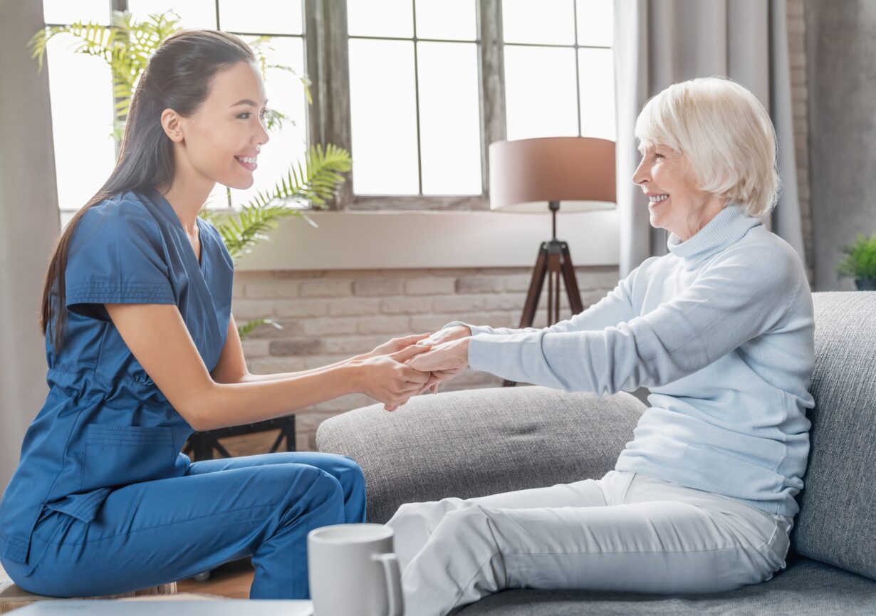 Assisting senior people. Female caregiver holding elderly woman's hands indoors