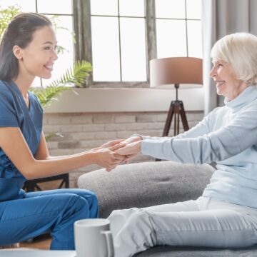 Assisting senior people. Female caregiver holding elderly woman's hands indoors