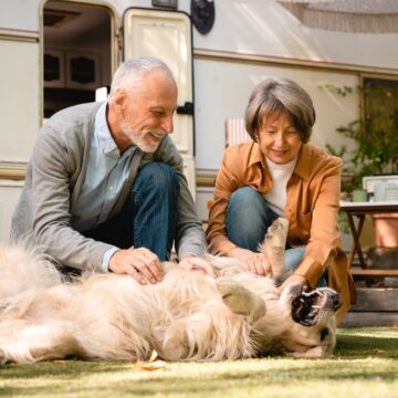 Caucasian senior couple playing walking their dog pet golden retriever together on porch of trailer