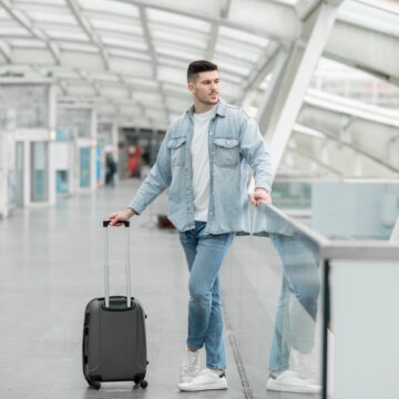 Male Passenger With Travel Suitcase Waiting For Flight In Airport