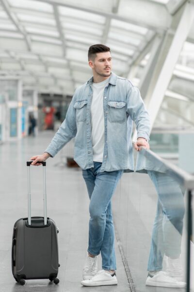 Male Passenger With Travel Suitcase Waiting For Flight In Airport