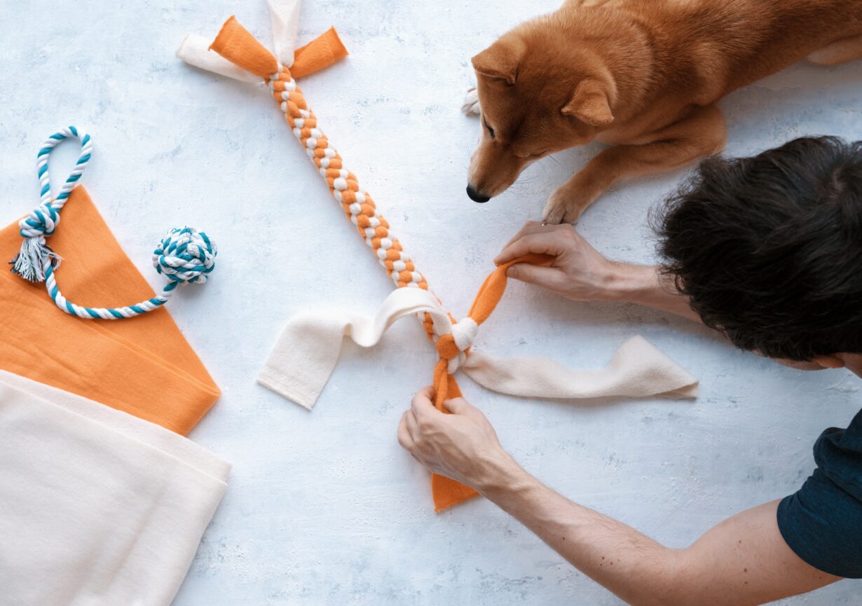 Top view of adult man making DIY homemade educational toys for dogs using fleece fabric stripes